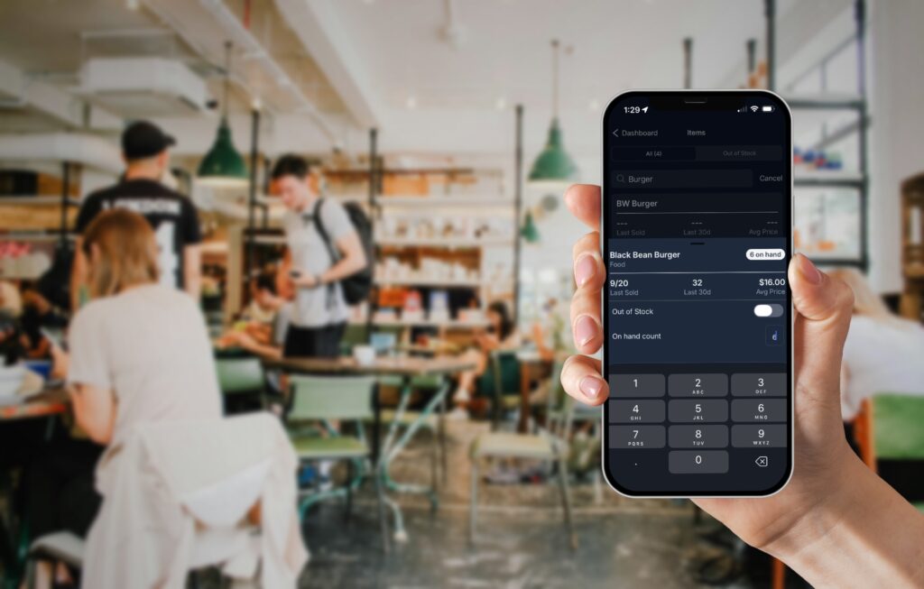 Manager holding their phone in a busy restaurant editing the on hand count of a menu item