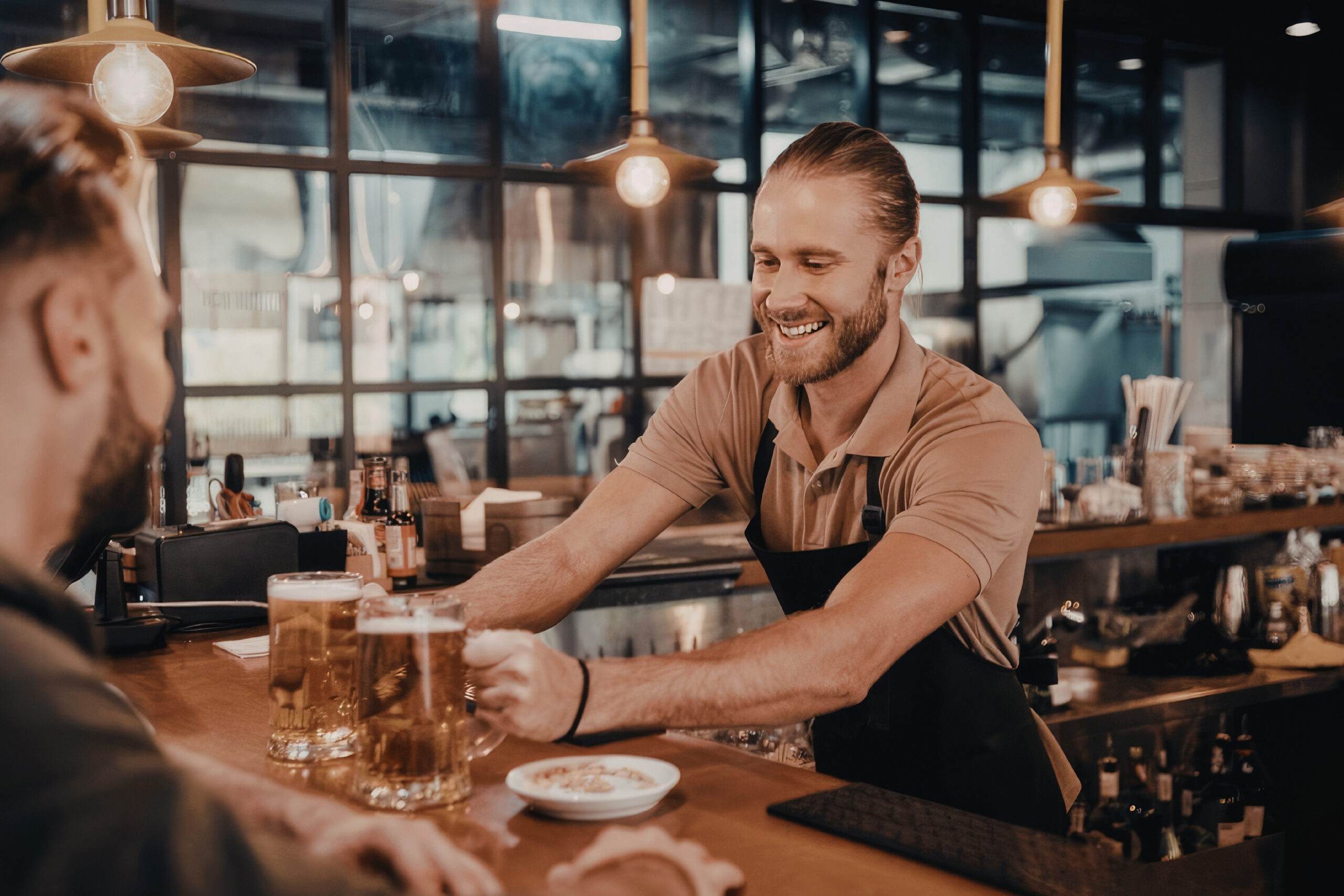 Loyalty guests sitting at a bar being served beers by a happy bartender.